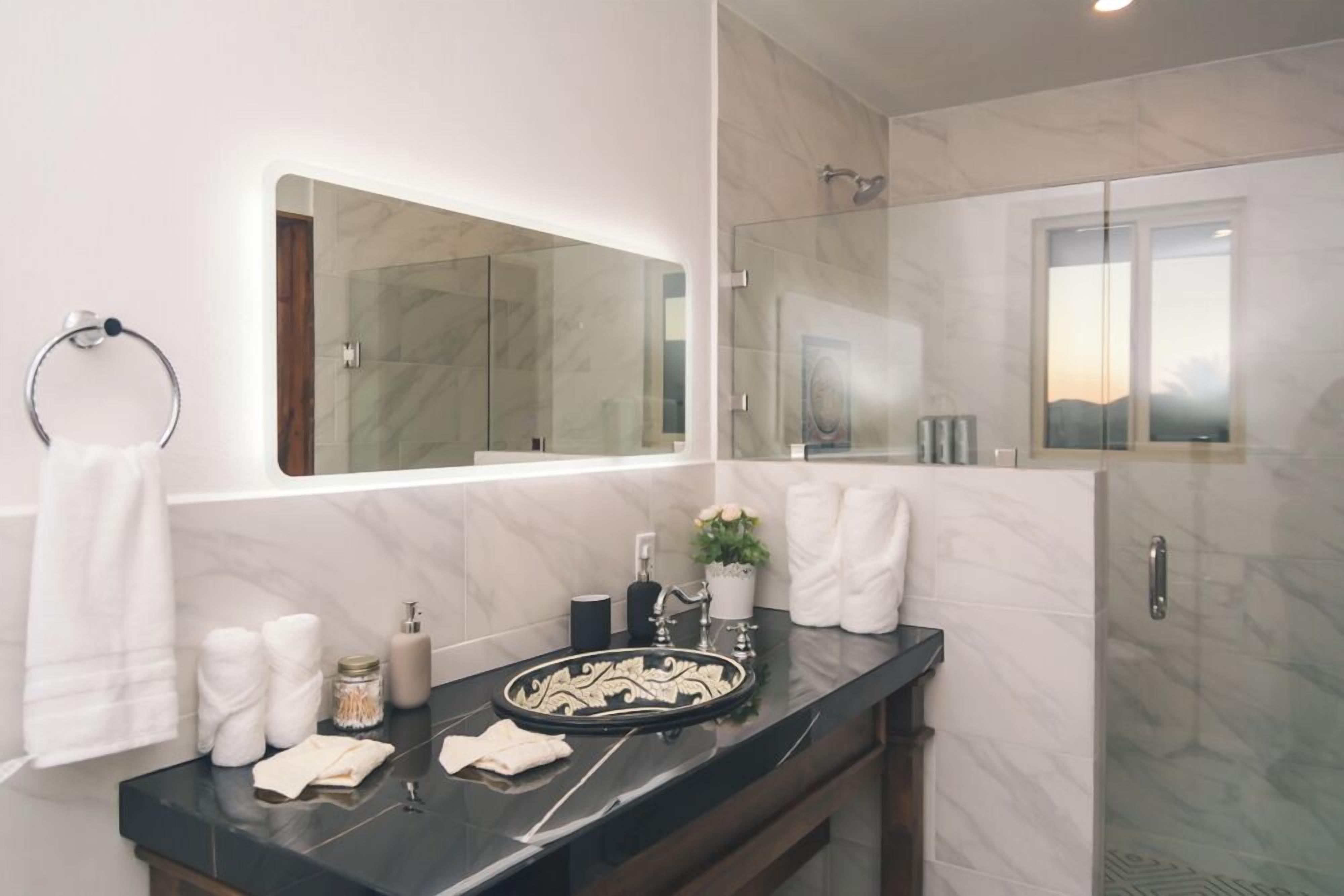 A modern bathroom with a marble vanity, a large mirror, and a glass shower enclosure.
