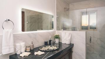 A modern bathroom with a marble vanity, a large mirror, and a glass shower enclosure.