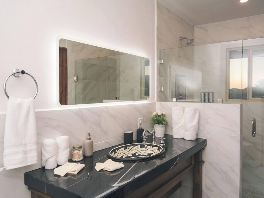 A modern bathroom with a marble vanity, a large mirror, and a glass shower enclosure.