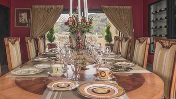 A formal dining room with a long table set for a meal, flanked by ornate chairs, and a wine rack in the background.