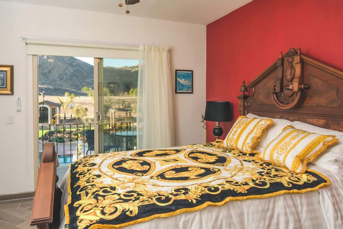 Une chambre à coucher avec un grand lit, une tête de lit en bois, une table de chevet et une vue sur un balcon avec une montagne en arrière-plan.
