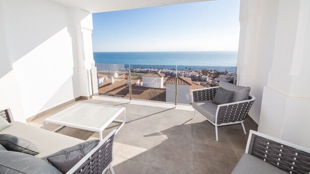 Un balcone con vista sul mare e sulla città, arredato con un divano, sedie e un tavolo.