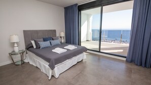 Una moderna camera d'albergo con un ampio letto e una porta vetrata che dà su un balcone con vista sul mare.