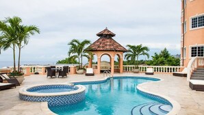 Uma piscina com um gazebo, palmeiras e vista para o oceano.