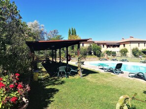 A pool area with lounge chairs, a covered seating area, and a building in the background. - Tuscan Charm at Caliano Villa (Asciano)