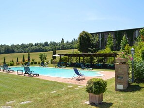 A swimming pool with lounge chairs and a covered seating area, surrounded by greenery and a view of hills. - Tuscan Charm at Caliano Villa (Asciano)
