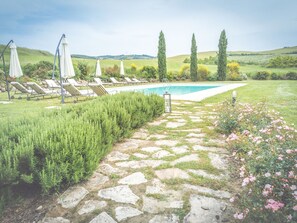A poolside area with lounge chairs and umbrellas, a stone pathway, and a view of the countryside. - Villa Gallina Grande Stay (Castiglione d'Orcia)