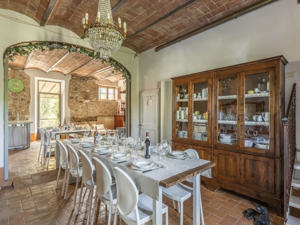 A dining area with a long table set for a meal, a wooden cabinet with glass doors, and a stone wall.