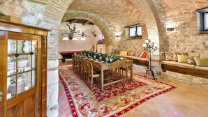 Un interno rustico con un arco in pietra, un'area pranzo con un tavolo lungo e sedie, e un divano con cuscini.