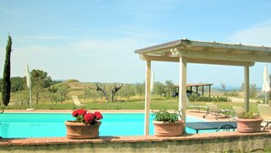 Un área de piscina con una pérgola, sillones de descanso y plantas en macetas.
