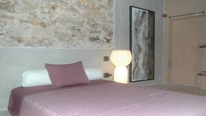 A bed with a pink quilt, a white pillow, and a purple pillow. There is a wall with a stone texture and a painting. - Belvilla by OYO Casaruscello (San Giuliano Terme)