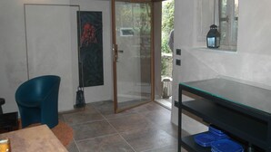 A modern room with a glass door leading to an outdoor area, a blue chair, a table with a glass, and a shelf with blue plates. - Belvilla by OYO Casaruscello (San Giuliano Terme)