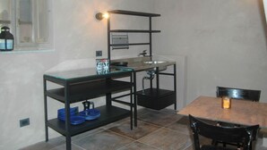 A compact kitchen with a glass-top table, black metal shelving, and a sink. - Belvilla by OYO Casaruscello (San Giuliano Terme)