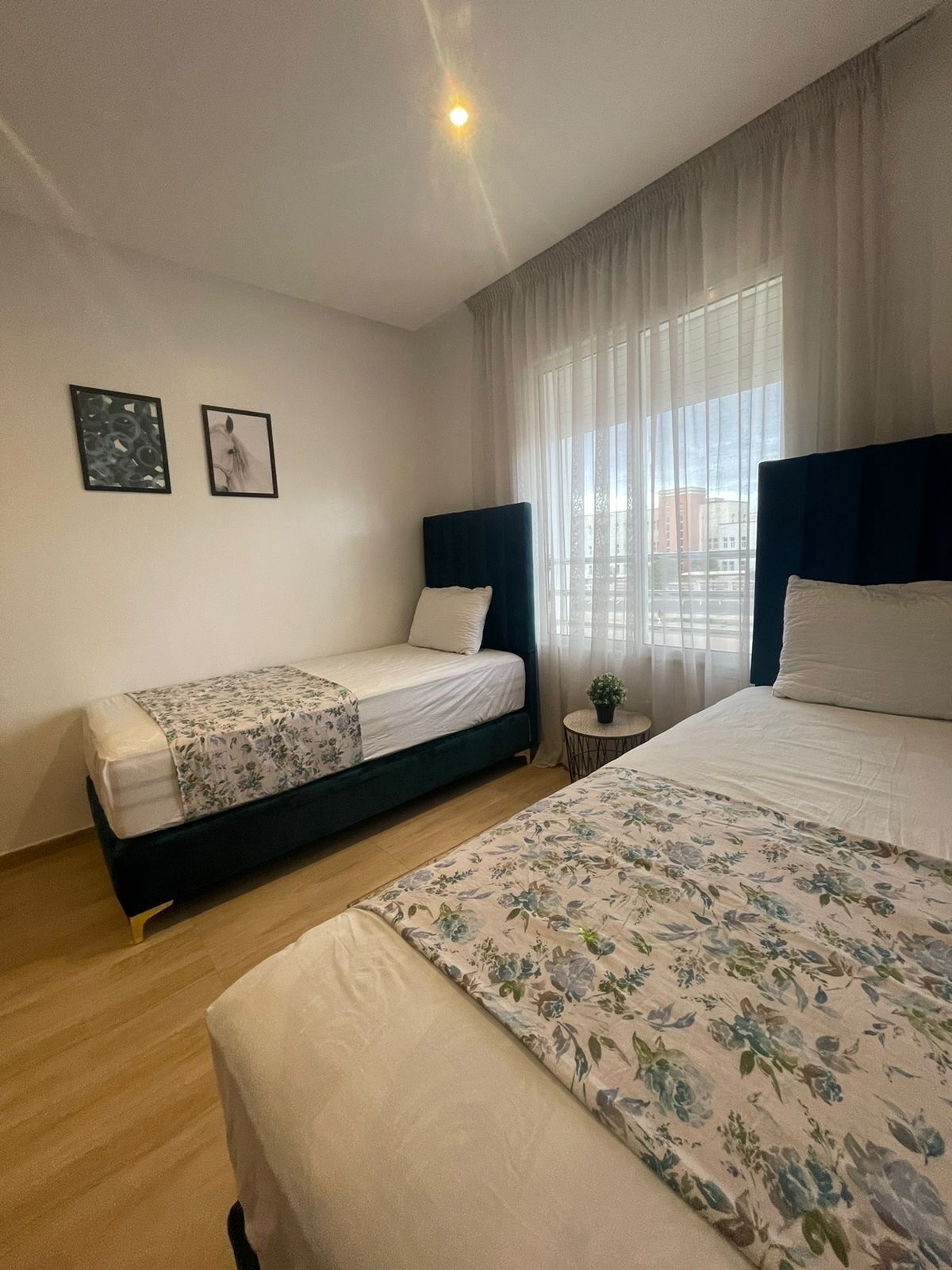 Ein Hotelzimmer mit zwei Betten, einem kleinen runden Tisch mit einer Pflanze und zwei gerahmten Bildern an der Wand.