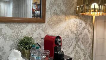 Una habitación con una mesa de madera, una cafetera roja, una planta en maceta, un espejo y una lámpara de pie.