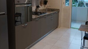 Une cuisine moderne équipée d’un four encastré, d’un réfrigérateur en acier inoxydable et d’une cuisinière à gaz. On peut voir une petite plante en pot sur le plan de travail et une fenêtre donnant sur la ville.
