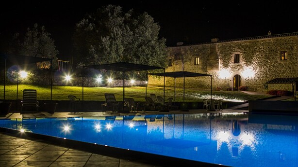 An outdoor swimming pool with lounge chairs and umbrellas, surrounded by stone buildings and trees. - Tasteful Countryside Stay (Montalcino)