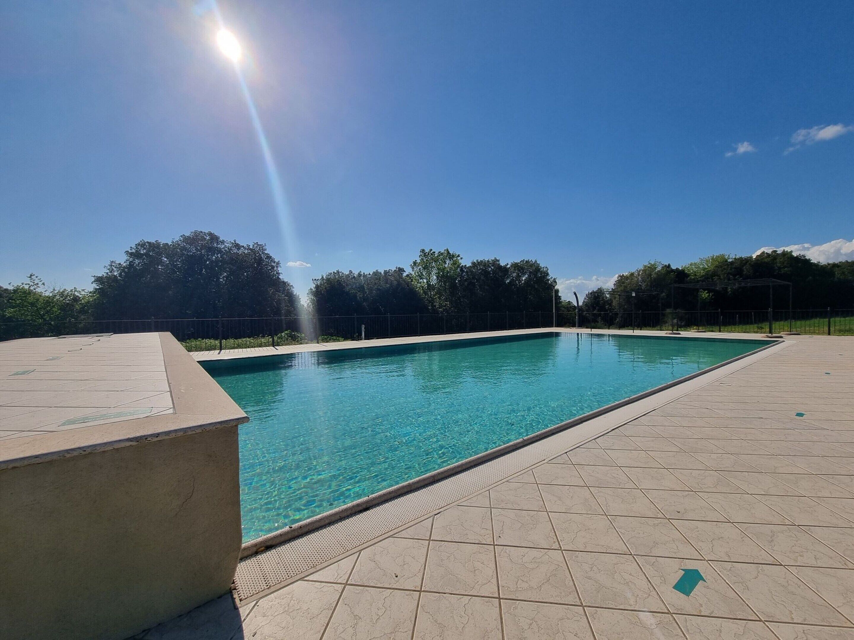 A rectangular swimming pool with clear blue water, surrounded by a tiled deck.