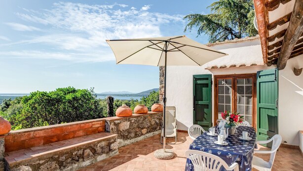 A patio with a table set for two, a large umbrella, and a view of the sea. - Tuscany Villa With Terrace (Orbetello)