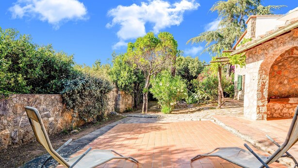 A patio with two sun loungers, a stone wall, and a building with a stone facade. - Tuscany Villa With Terrace (Orbetello)