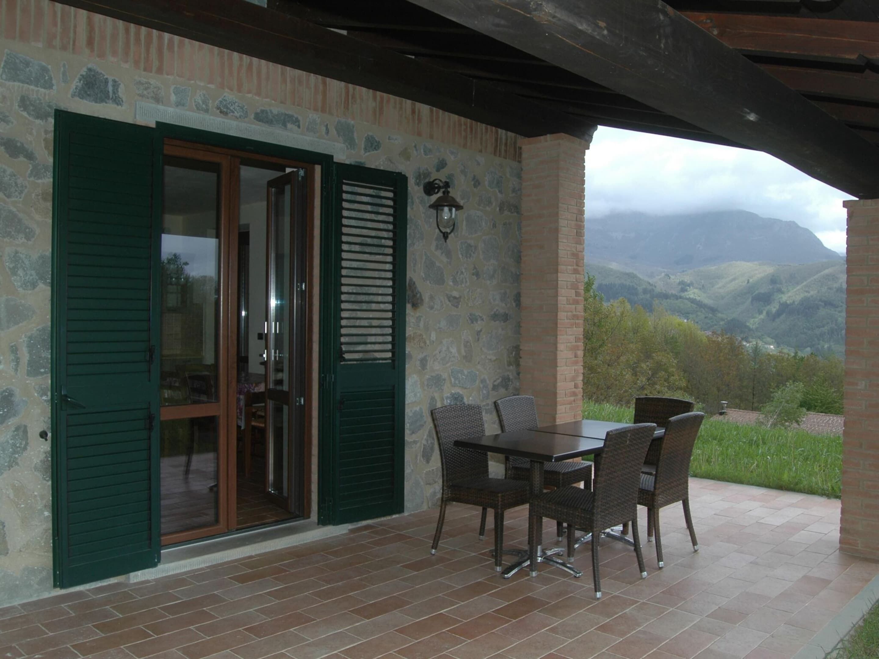 Eine Terrasse mit Tisch und Stühlen, eine Steinmauer und Blick auf Berge.