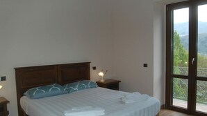 A bedroom with a large bed, a nightstand with a lamp, and a view of a mountainous landscape through a sliding glass door. - Holiday Home With Pool in Camporgiano (Camporgiano)
