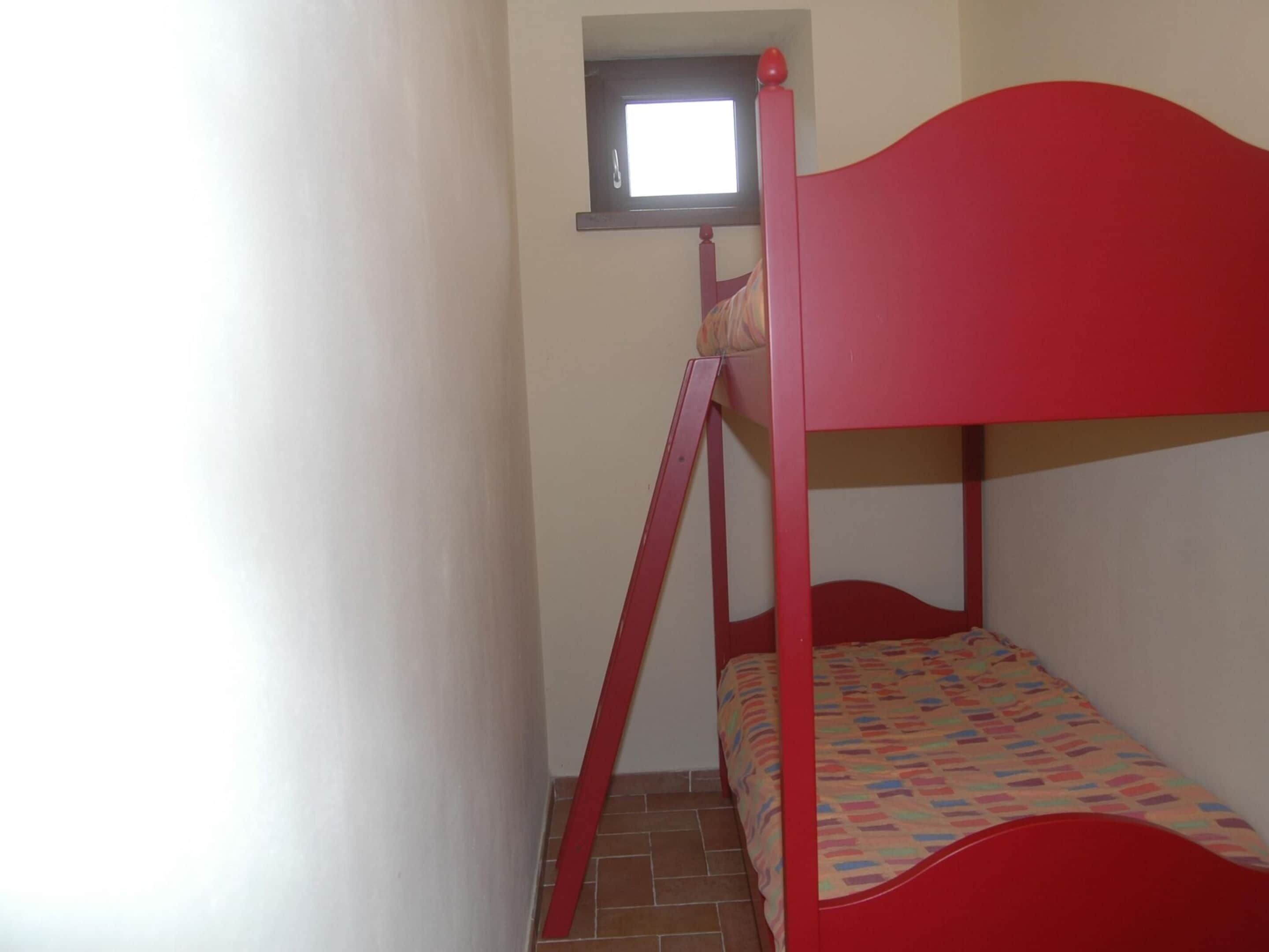 Habitació petita i estreta amb una llitera vermella i una finestra a dalt.