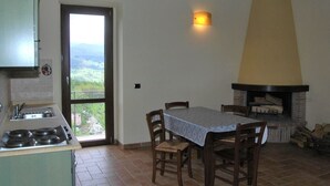 A kitchen with a stove, sink, and a dining area with a table and chairs. There is a fireplace and a view of the outdoors through a door. - Holiday Home With Pool in Camporgiano (Camporgiano)