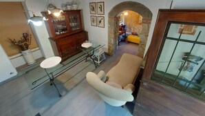Une pièce chaleureuse avec un plafond en bois, une table en verre, un fauteuil rembourré, une arche en pierre et un buffet en bois doté de portes en verre.