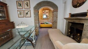 Un salon chaleureux avec une table à manger en verre, un canapé, une cheminée et une arche en pierre qui mène à une autre pièce.