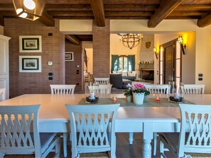 A dining area with a long table and white chairs, a fireplace, and a chandelier. - Peccioli Countryside Villa (Peccioli)