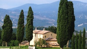 A rustic villa with a tiled roof, surrounded by tall cypress trees, set against a backdrop of rolling hills and mountains. - Holiday Home in Celle Sul Rigo With Swimming Pool (San Casciano dei Bagni)