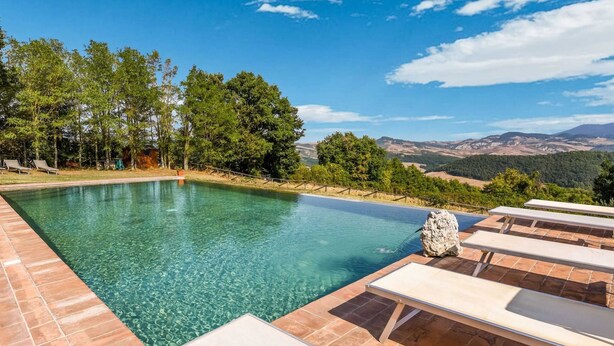 A clear swimming pool with tiled edges, surrounded by lounge chairs and a view of a mountainous landscape. - Holiday Home in Celle Sul Rigo With Swimming Pool (San Casciano dei Bagni)