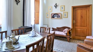 Una sala de estar acogedora con un sofá de madera, una mesa de comedor con sillas, una mesa de centro y una chimenea. Hay cuadros enmarcados en la pared y una puerta de madera.