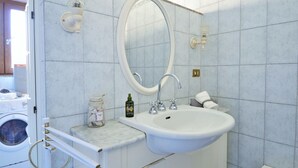 Un baño con lavamanos blanco, un espejo y una lavadora al fondo.