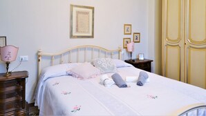 Una cama bien hecha con una colcha estampada, una lámpara de noche y una mesita con un cuadro enmarcado.