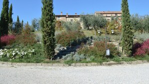 A traditional stone building with a tiled roof, surrounded by a well-maintained garden with various shrubs and flowers. - Apartment in Tuscany With Stunning Views (Asciano)