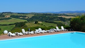 A pool with white lounge chairs and a clear view of rolling hills and distant mountains. - Apartment in Tuscany With Stunning Views (Asciano)