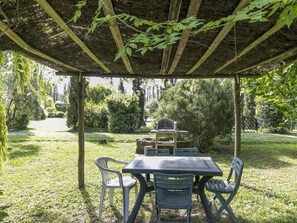 Une terrasse extérieure avec une table et des chaises, un barbecue et une structure en forme de pergola.