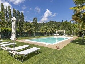 Une piscine rectangulaire, agrémentée de chaises longues et de parasols, entourée d’une pelouse et d’arbres.