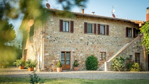 A stone building with a wooden door, multiple windows with shutters, and a gravel driveway. - Modern Vacation Home (Pienza)