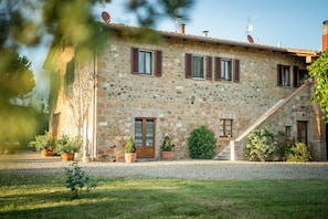 A stone building with a wooden door, multiple windows with shutters, and a gravel driveway. - Modern Vacation Home (Pienza)