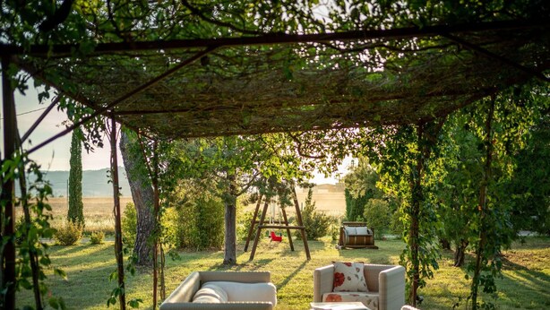 A covered outdoor seating area with wicker furniture and a swing set. - Modern Vacation Home (Pienza)