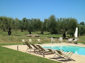 A pool area with lounge chairs and umbrellas, surrounded by trees and a grassy field. - Belvilla by OYO Villa Le Buche (Sarteano)