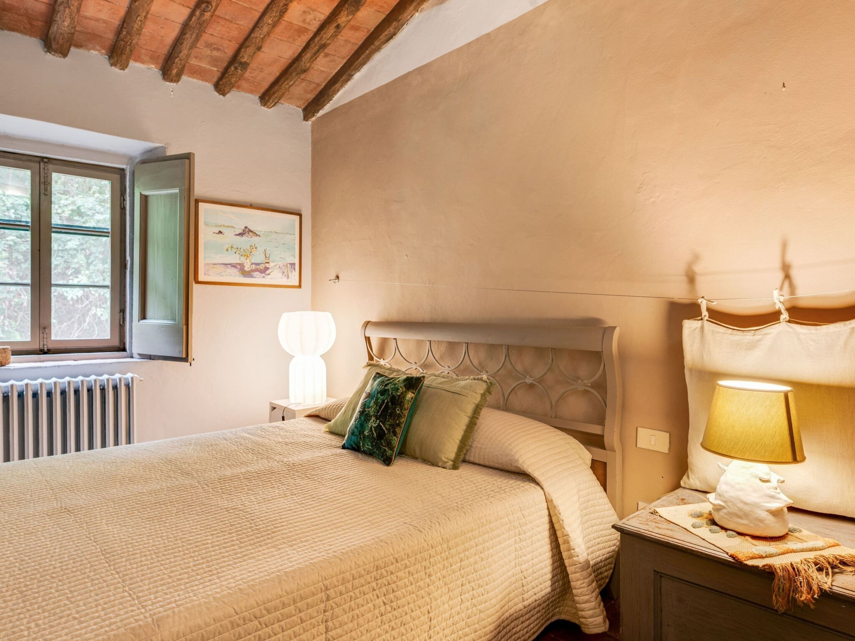 A bedroom with a bed, a nightstand, a lamp, a window, and a radiator.