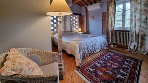 Quarto aconchegante com cama, cadeira de vime, luminária de chão e tapete estampado.
