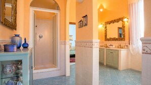 A hallway with a glass display case of teapots, a door leading to another room, and a bathroom with a large mirror and green cabinets. - Lavish Villa in Peccioli (Peccioli)