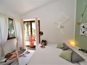 A bedroom with a bed, pillows, a hanging light fixture, a suitcase, and a door leading to an outdoor area.