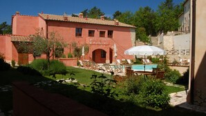 A red villa with a swimming pool, outdoor seating, and a garden.