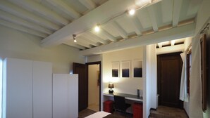 A bedroom with a bed, a desk, and a chair. There are two doors, one leading to a bathroom and another to a hallway.